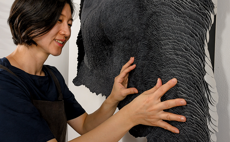 Yong Joo Kim in front of her work, Weight of Commitment: 4 Years Old